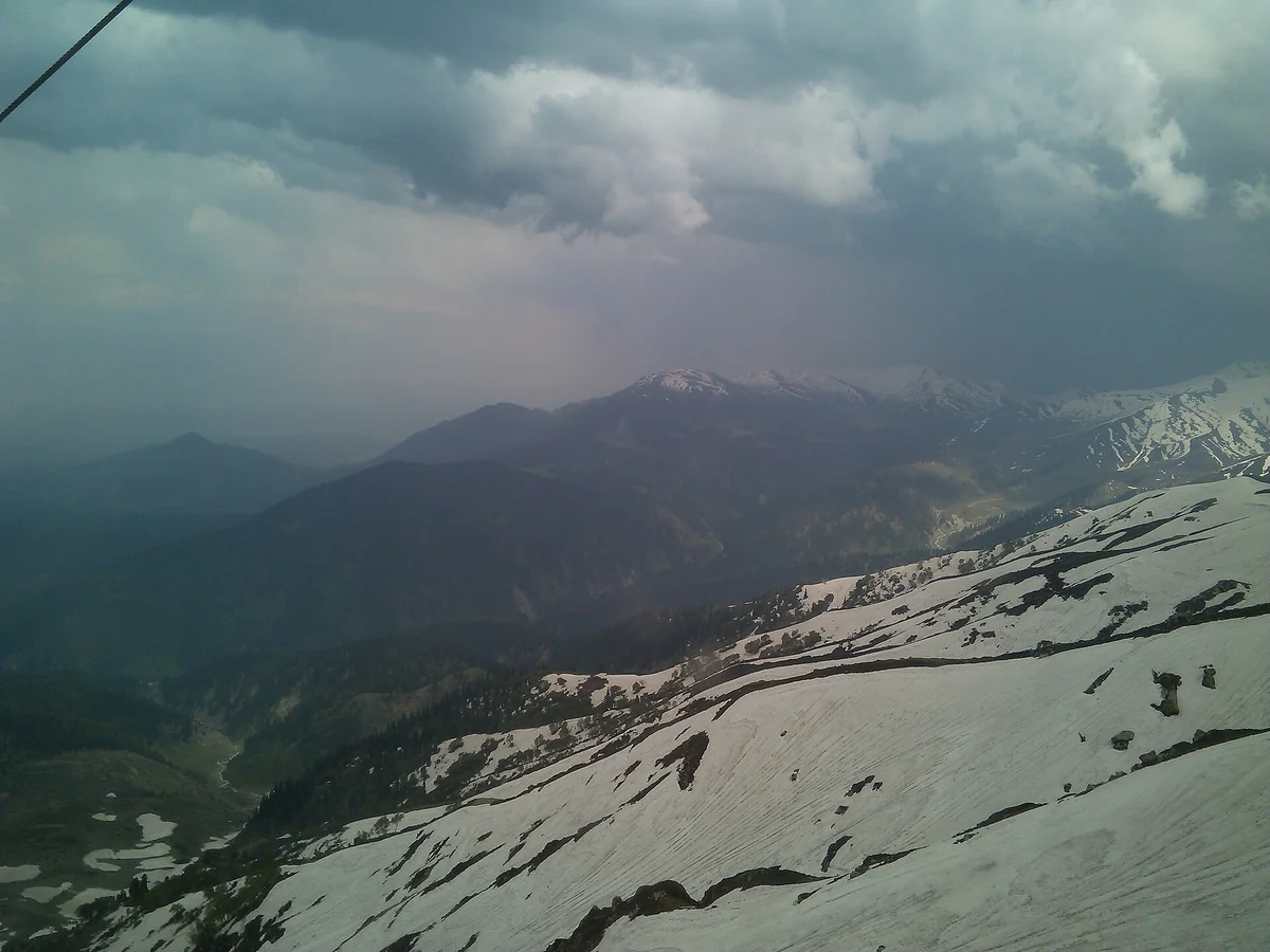 Snow-streaked mountain slopes above Pahalgam under a stormy sky