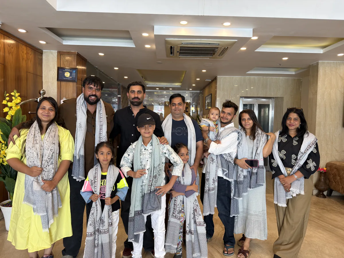 A family group with children in a hotel lobby with Zahid and another host, most of them wearing grey and white printed Kashmiri stoles