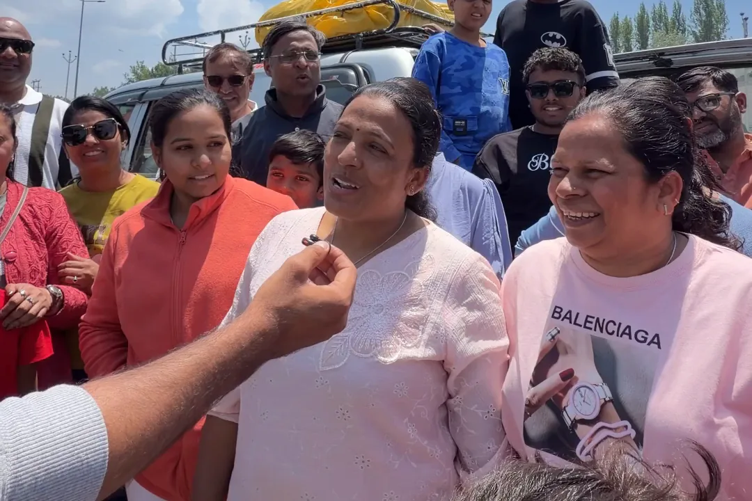 A woman in a pale pink kurta speaking into Zahid's microphone, surrounded by her Gujarati family group beside their car after a day in Gurez