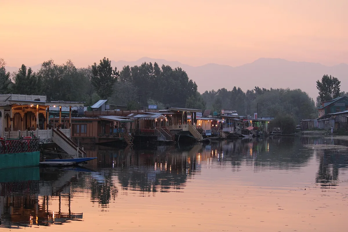Houseboats lit up at dusk on Dal Lake in Srinagar, reflected in still water with mountains behind