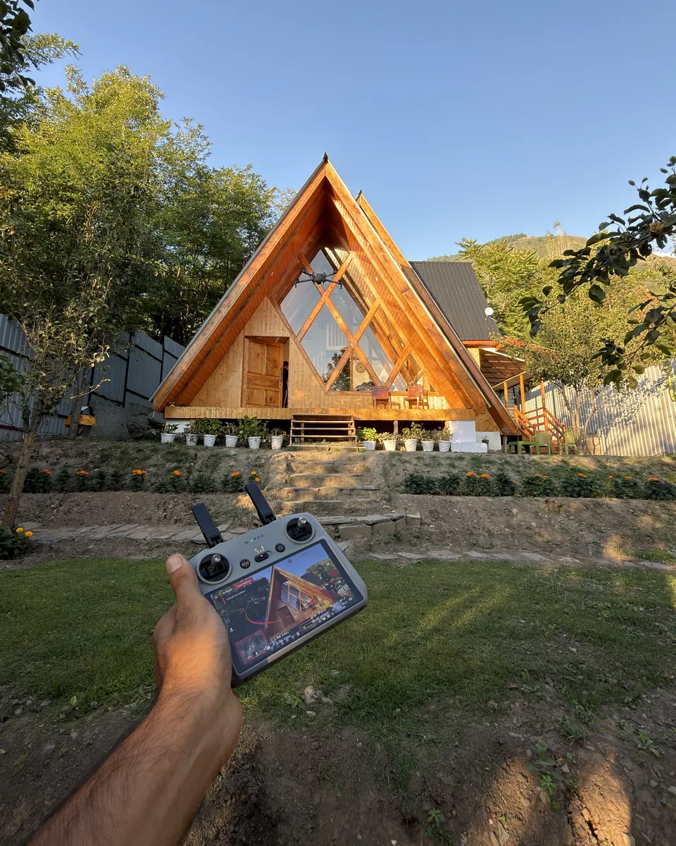 Wooden A-frame cottage near Dachigam, 12 km from Lal Chowk in Srinagar, with a drone controller in the foreground