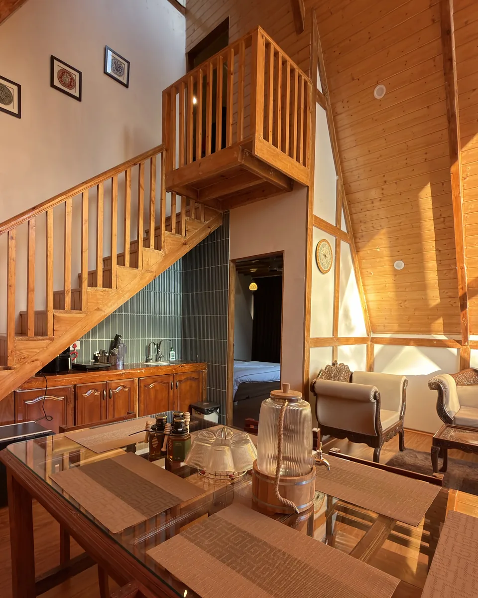 Inside the Srinagar A-frame cottage: wooden loft stairs, open kitchen, dining table and a view into the bedroom