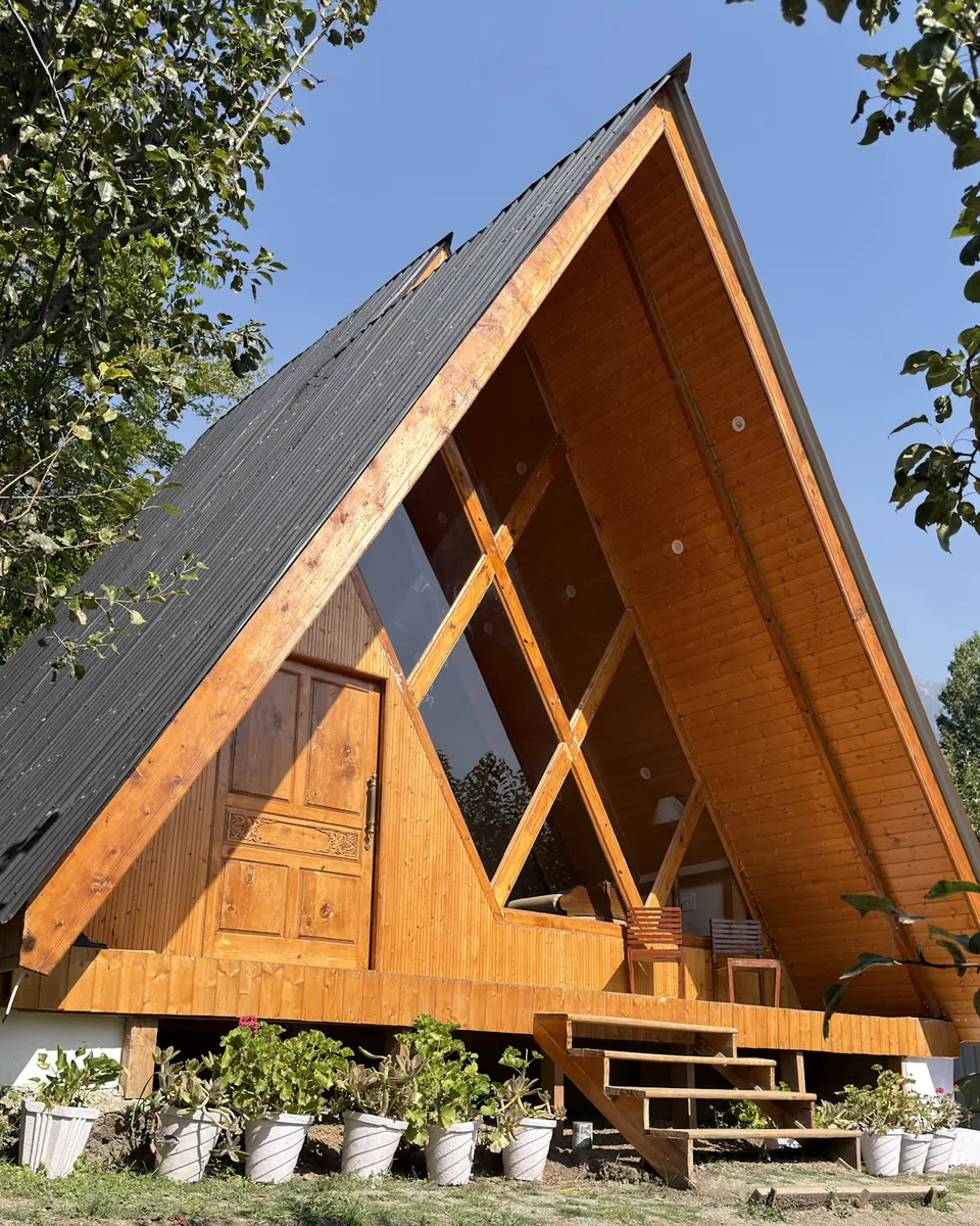 Front of the wooden A-frame cottage near Dachigam with its glass gable, deck chairs and potted plants