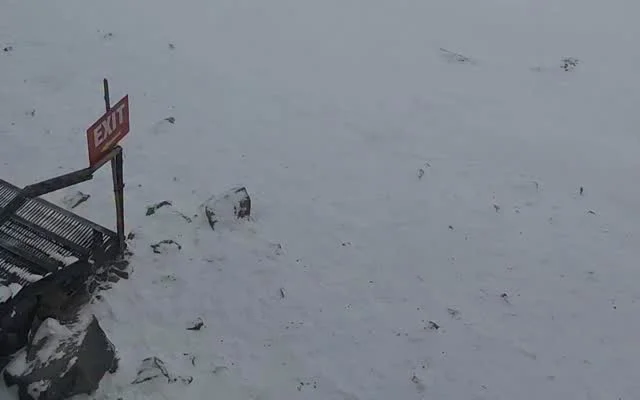 Fresh snow covering rocky ground at Gulmarg Gondola Phase 2 on 28 September 2026, with a red EXIT sign and a metal railing in the corner