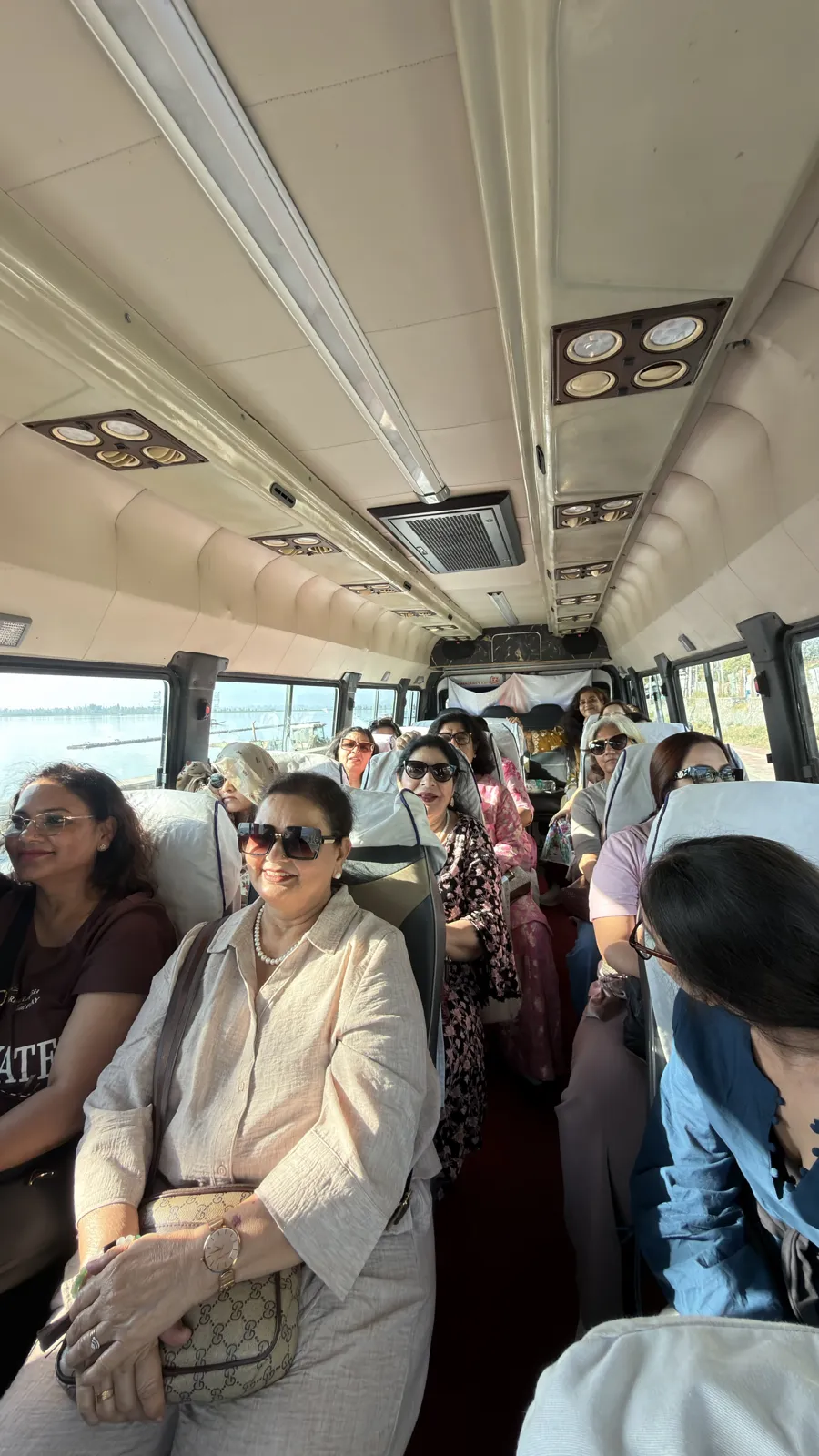 Women from our ladies group smiling in their seats inside an air-conditioned mini bus beside Dal Lake