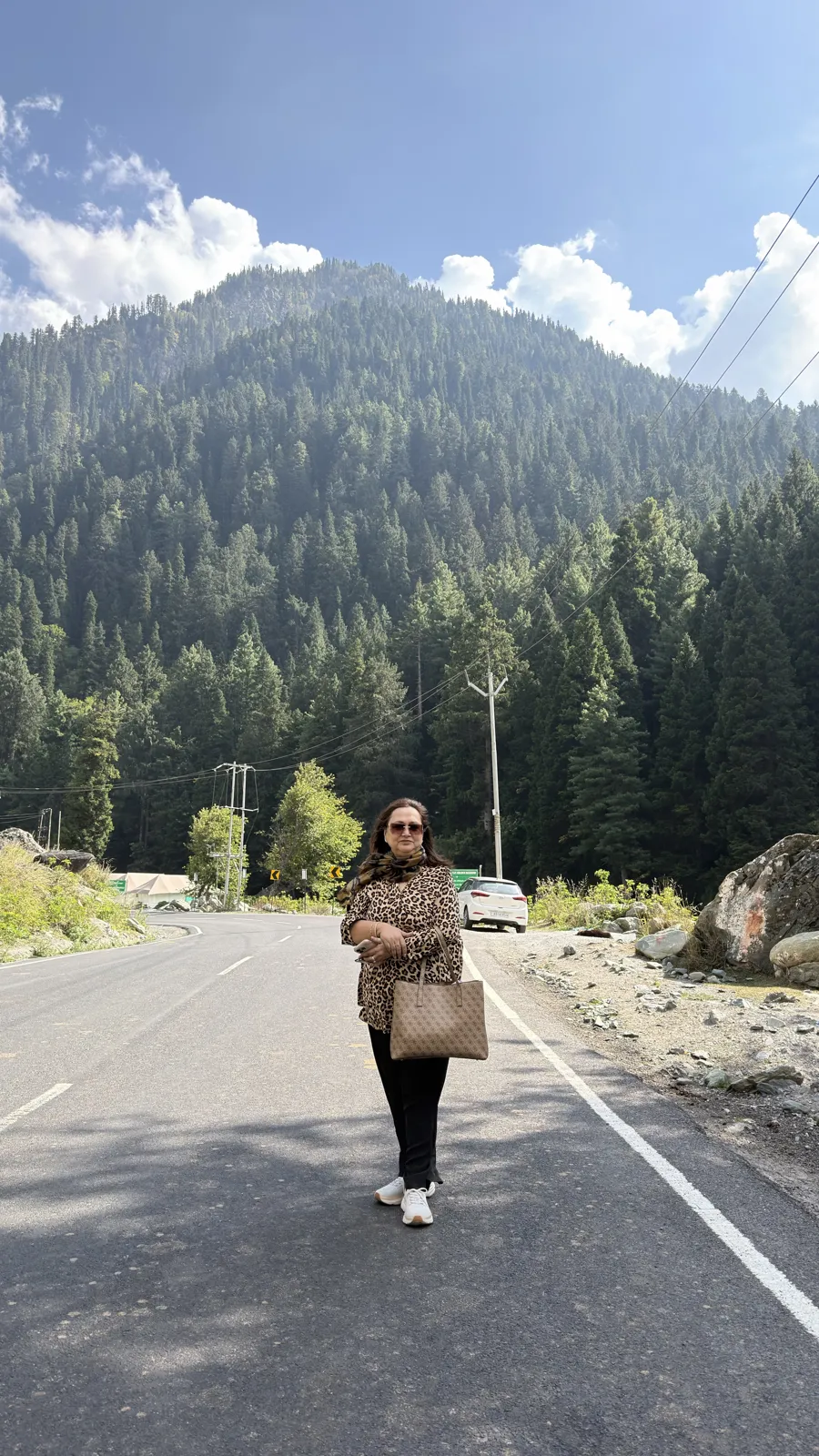 A guest from our ladies group in a leopard-print top, scarf and sneakers on a sunny mountain road lined with pine forest