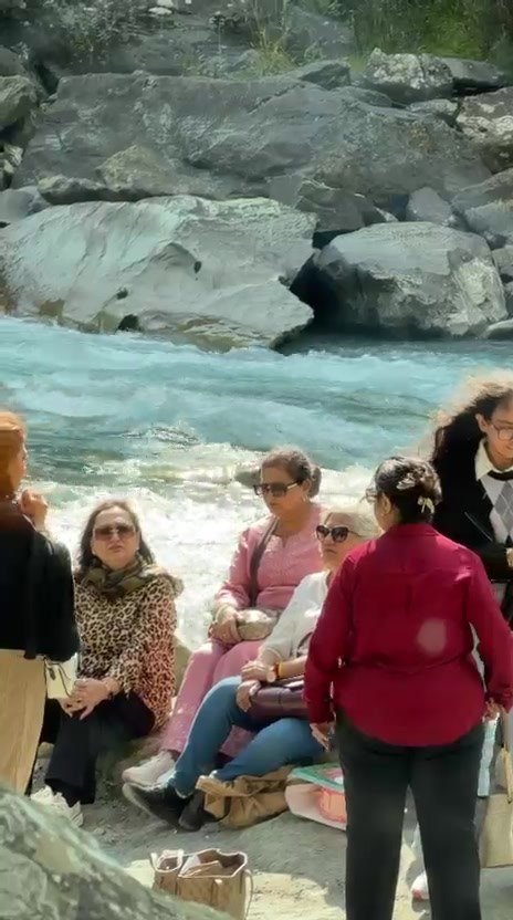 A group of women sitting on rocks right beside a fast, turquoise river, with large grey boulders on the far bank
