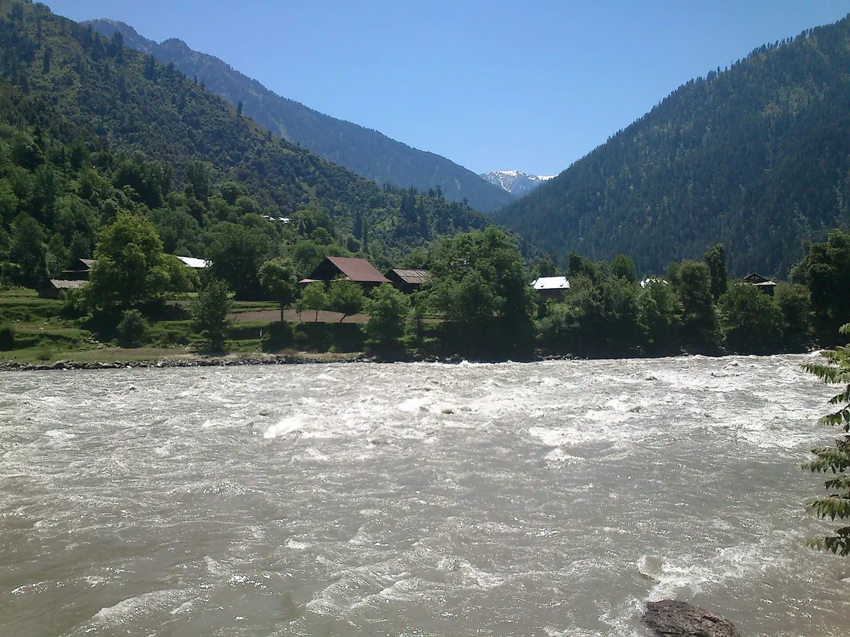 Houses and trees of Keran on the Indian bank of the Kishanganga river, with snow on a peak at the head of the valley
