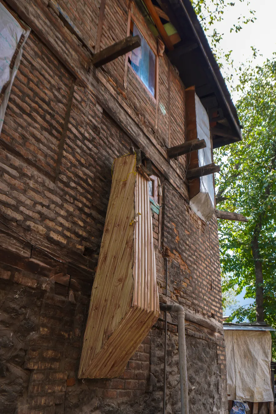 Brick house in Pahalgam with a carved wooden window box and a wooden chimney on its upper floor