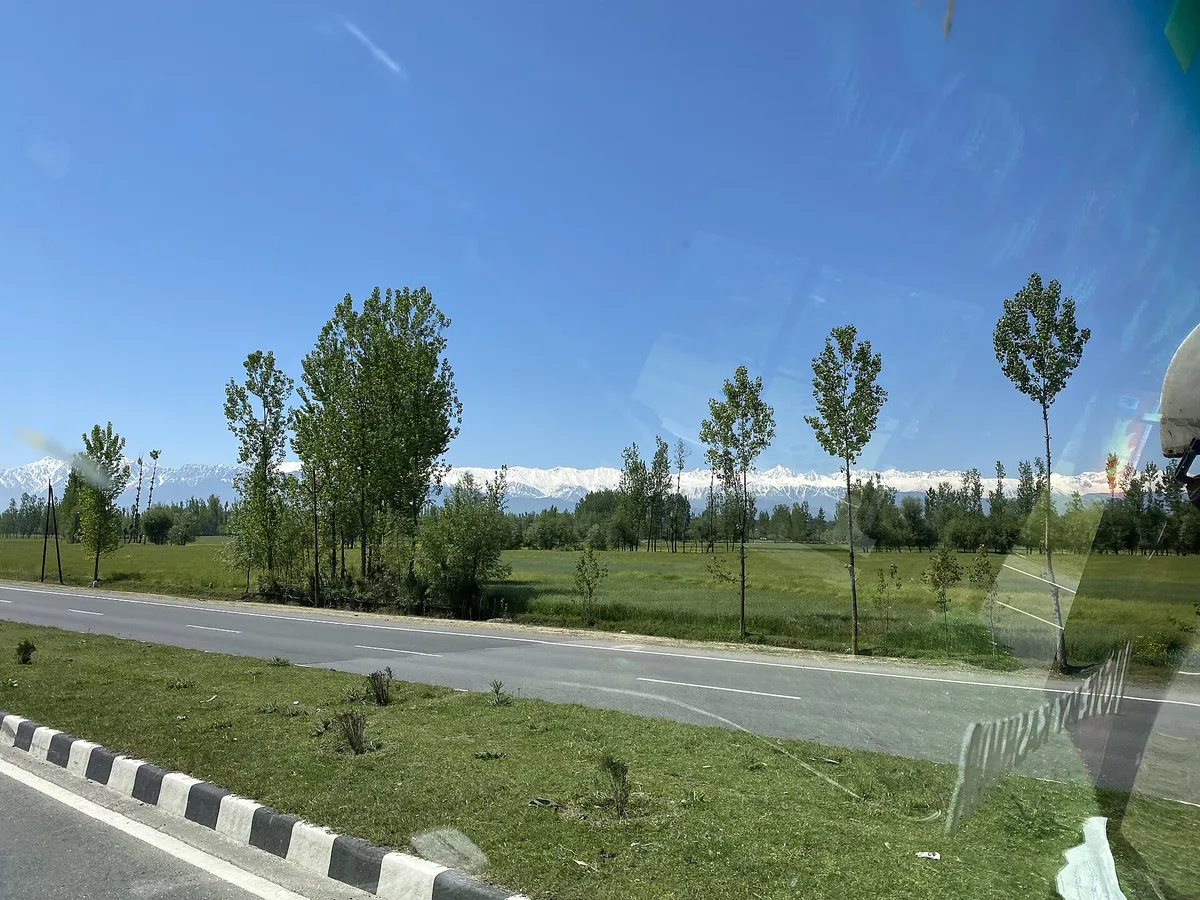 The Jammu to Srinagar highway, NH 44, near Bijbehara in Anantnag district, with green fields, tall trees and snow on the mountains behind