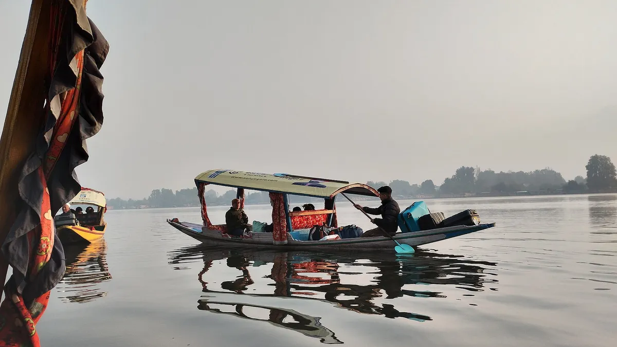 A shikara with passengers crossing Nigeen Lake on a hazy October morning, with trees on the far bank