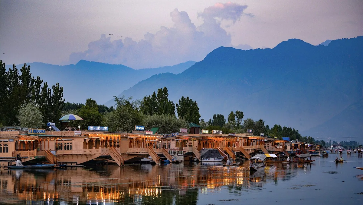 Houseboats lit at twilight along southwestern Dal Lake in Srinagar, photographed from Boulevard Road, with mountains behind