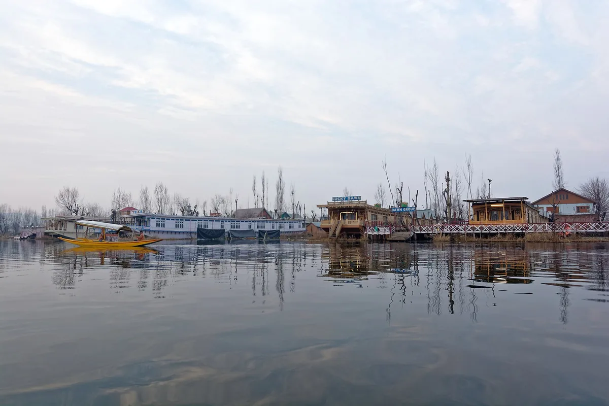 Wooden houseboats along Dal Lake in Srinagar on a grey winter day, with a yellow shikara on the water