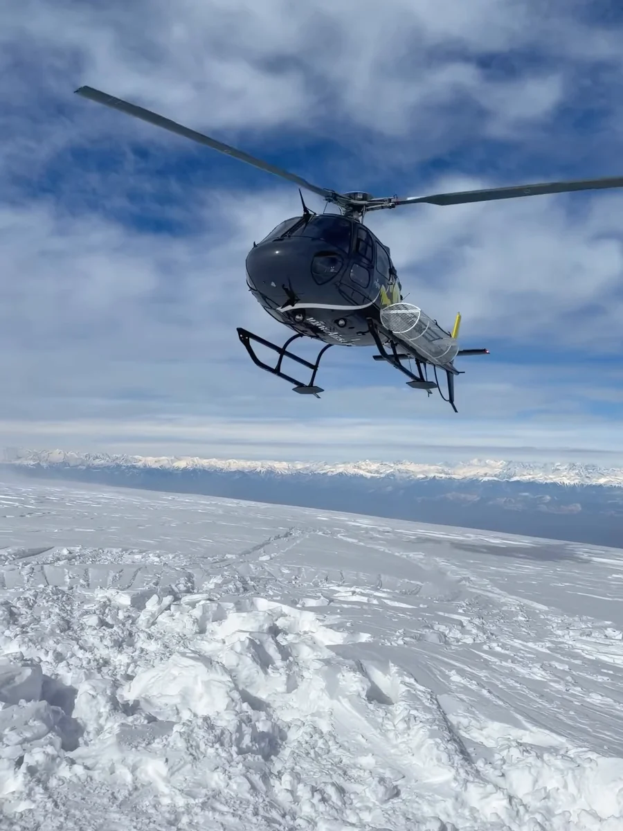 A black and yellow helicopter hovering low over deep snow at Gulmarg, from our reel