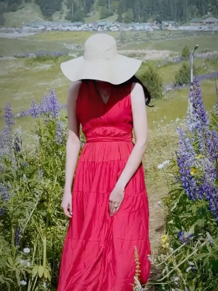 Our guest in a sun hat at the edge of the open Gulmarg meadow with pine forest behind, lupins in front