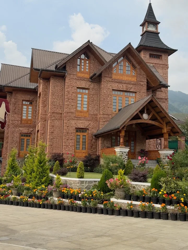 The red-brick tower resort in Srinagar from our reels, with its pointed tower, gabled roofs and flower beds in daylight