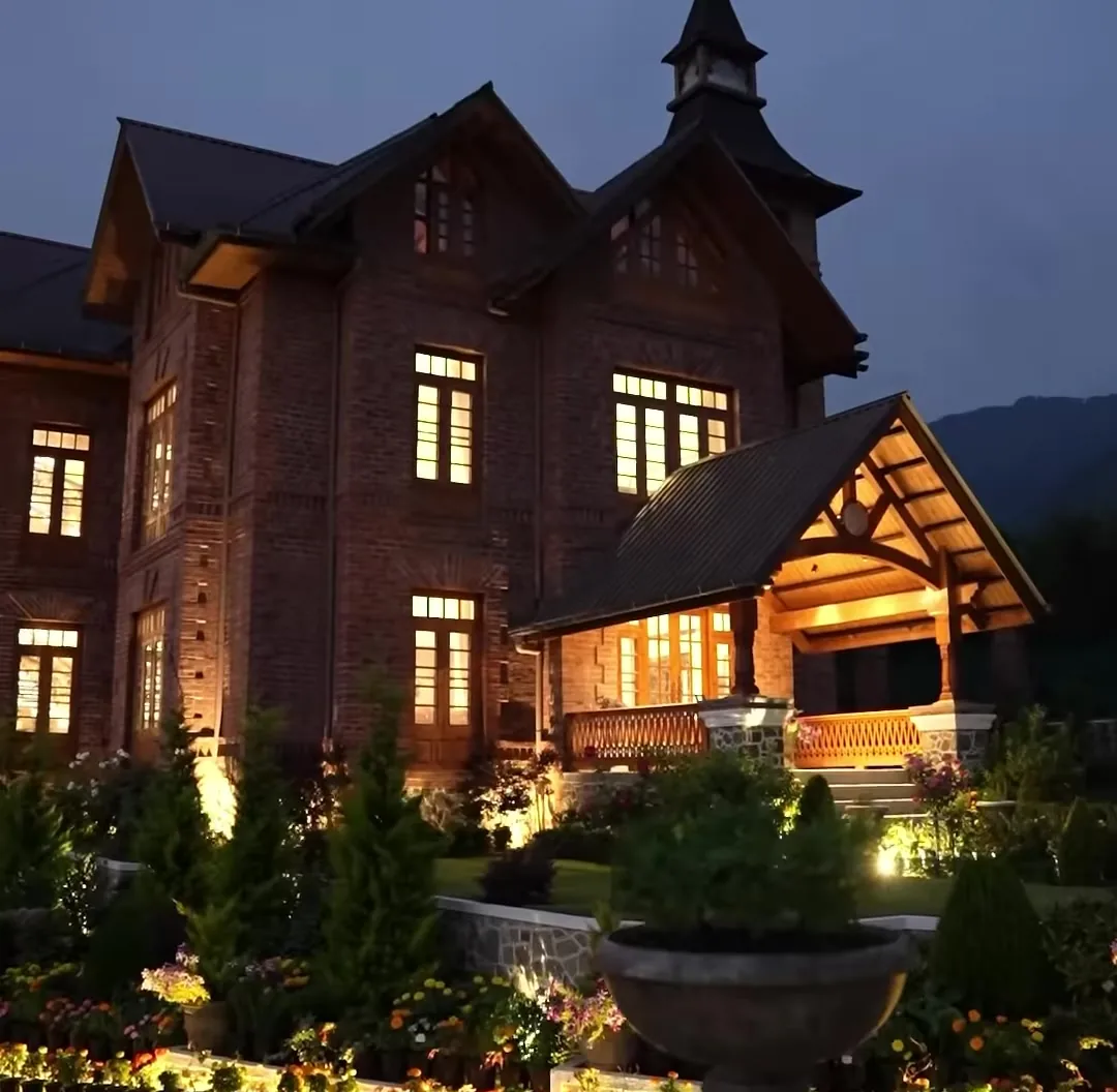The red-brick tower resort lit up at dusk, warm lights in the windows and along the garden