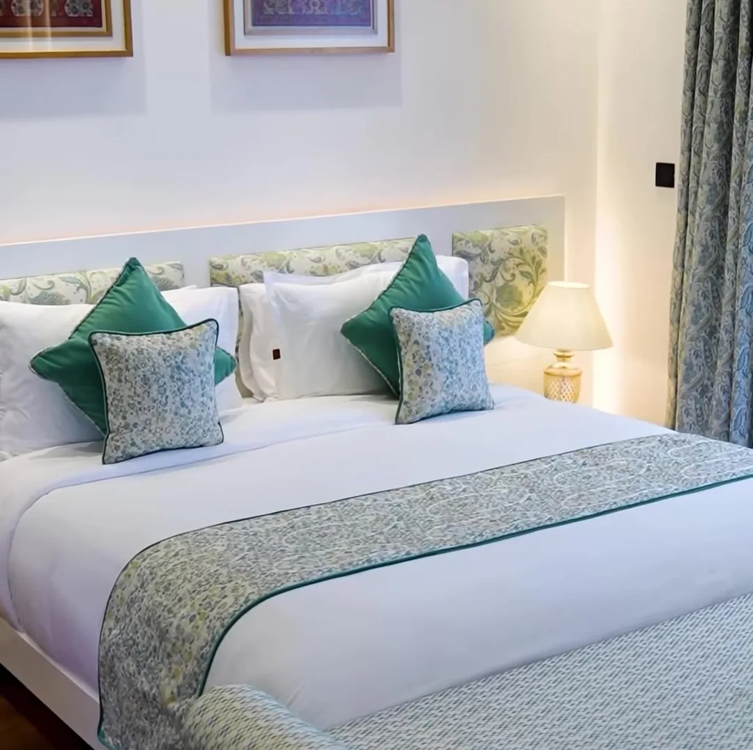 A bright double bedroom at the red-brick resort in Srinagar, with white bedding, green cushions and framed art