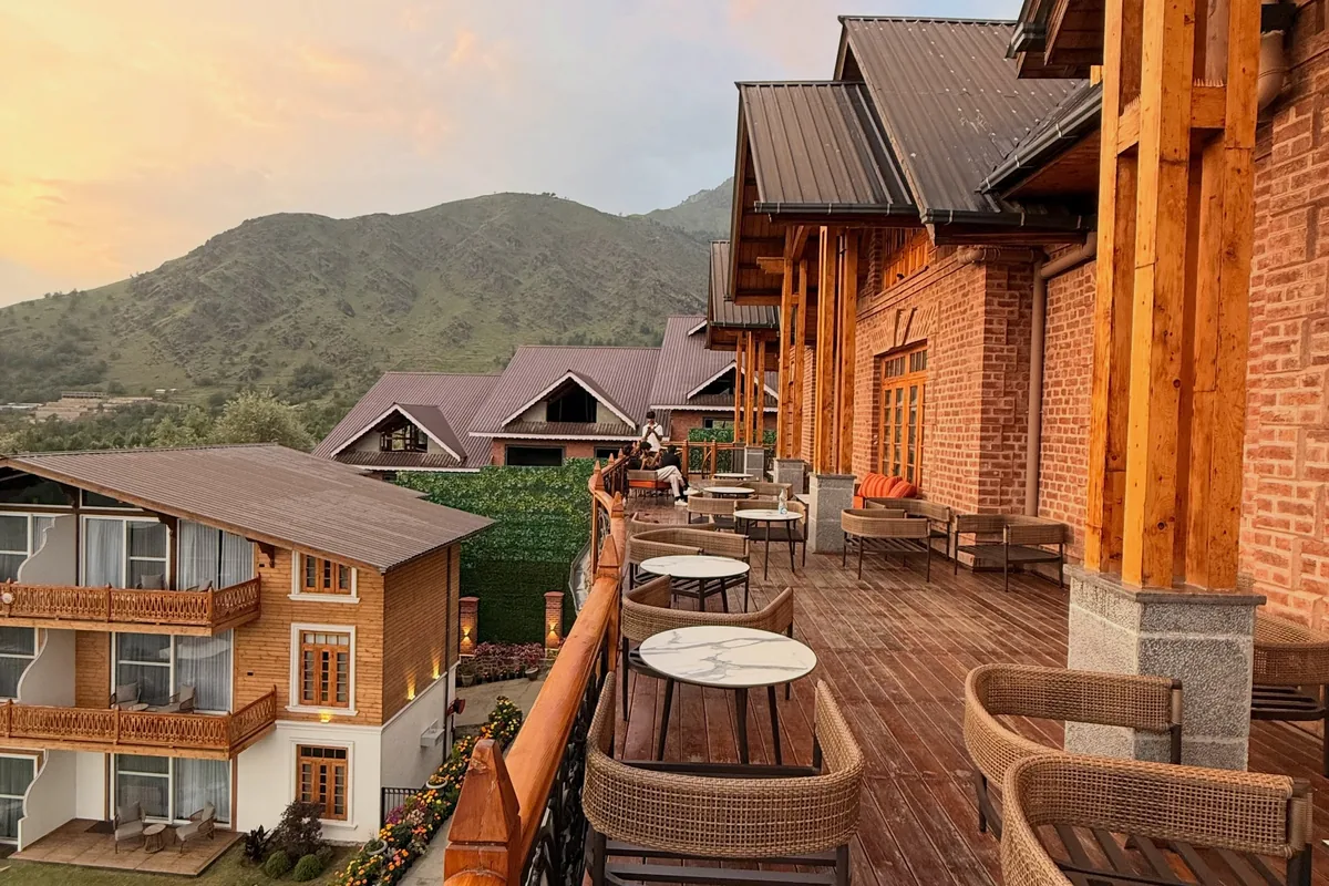 Wooden terrace with cane chairs at the red-brick resort, guest wings and green mountains behind at sunset