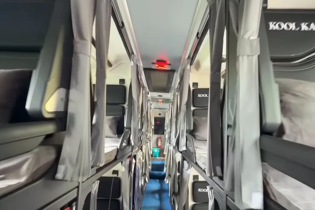 Inside a sleeper Volvo bus: upper and lower berths with curtains on both sides of a narrow blue-lit aisle