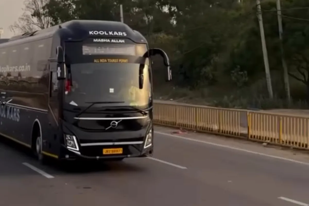 Front of a black sleeper Volvo bus driving on the highway with trees behind