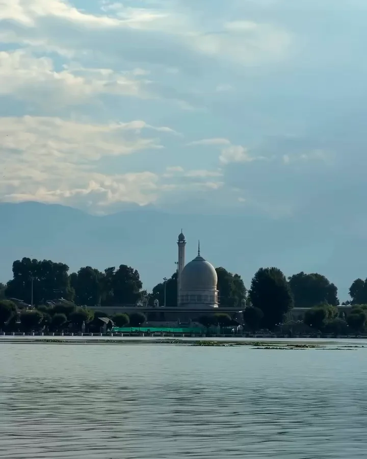 The white dome and minaret of Hazratbal Shrine across Dal Lake, under a big sky of white clouds with hazy mountains behind
