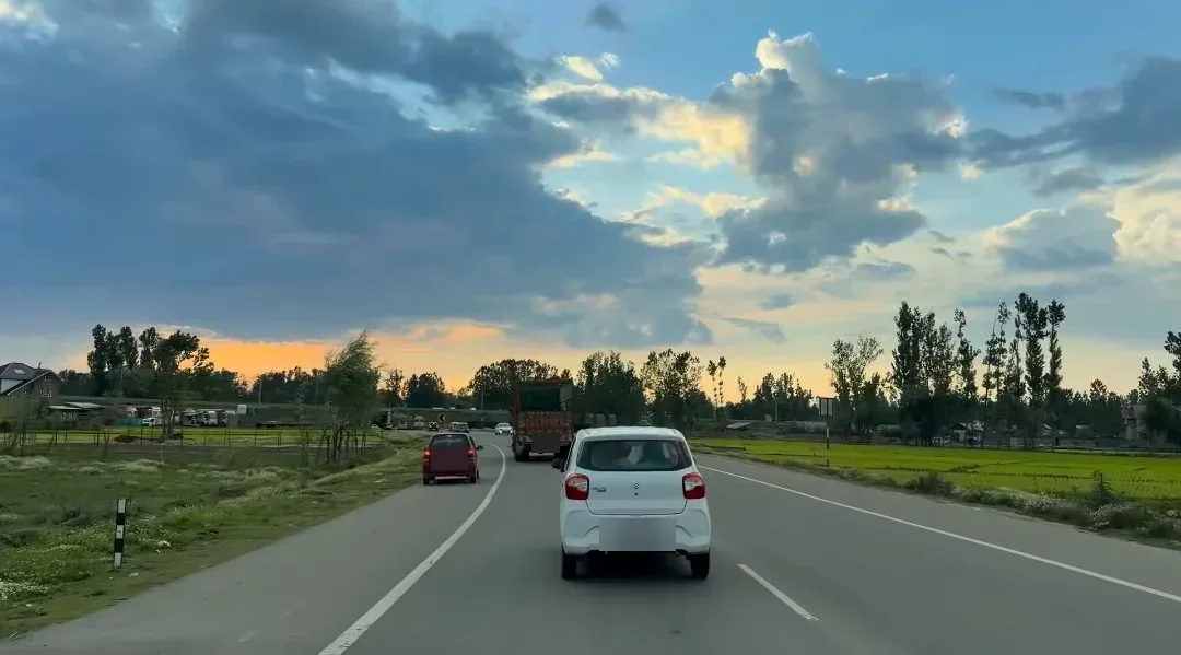 Cars on a four-lane highway through flat green fields in the Kashmir valley in the evening