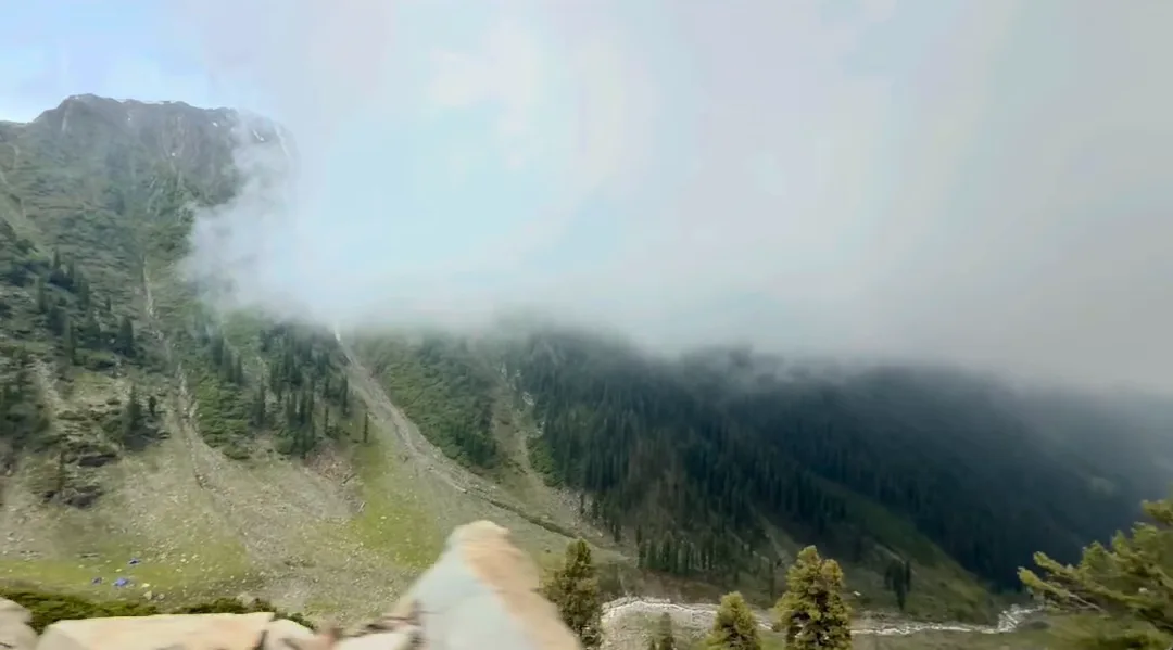 Low clouds rolling over green mountain slopes beside a road in Kashmir