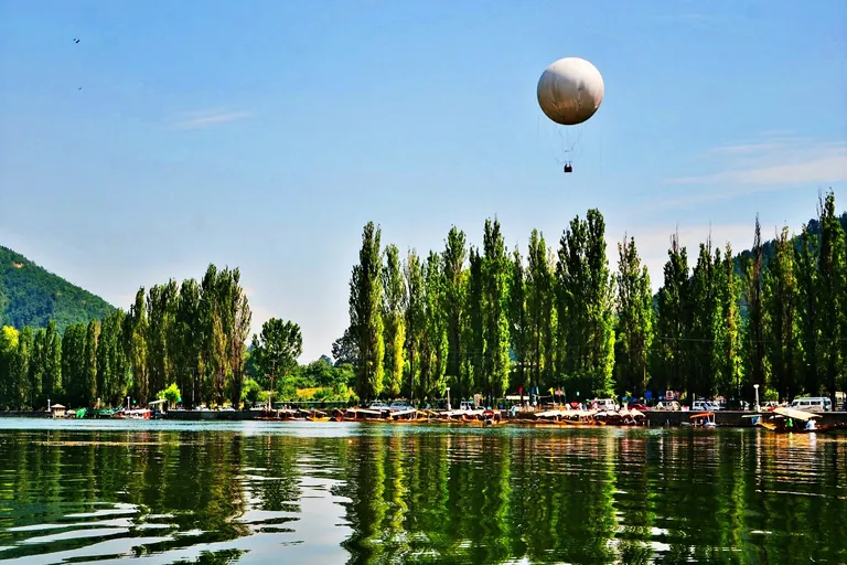 Tethered passenger balloon above the poplar-lined Dal Lake shore in Srinagar, seen from a boat